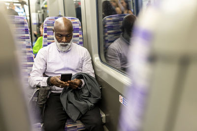 Bald senior businessman using mobile phone in train