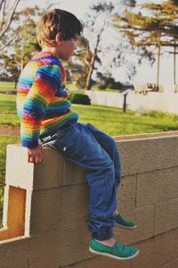 Side view of boy sitting on retaining wall