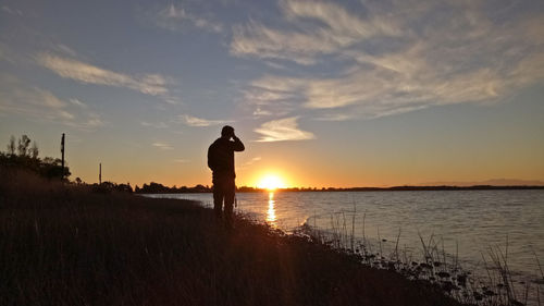 Silhouette man standing on beach against sky during sunset