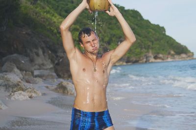 Shirtless mid adult man bathing with coconut water at beach