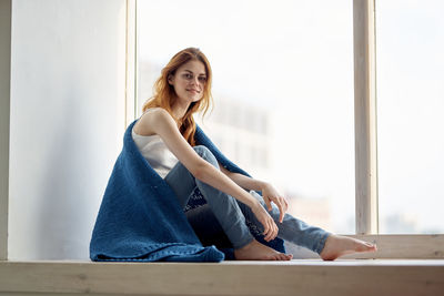 Portrait of young woman sitting on window