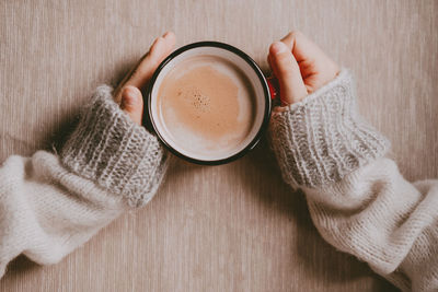 Hands in a sweater hold hot cocoa, in a red mug, top view. a cozy photo with a mug in hand