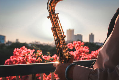 Midsection of girl playing saxophone in city against sky