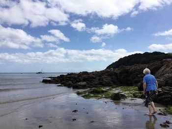 Rear view of woman standing on beach against sky