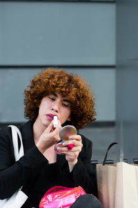 A non-binary person applies makeup sitting on a bench