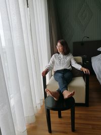 Young woman sitting on chair by window at home