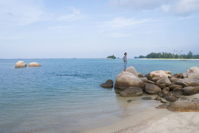 Mid distance view of man standing on rock at beach against sky