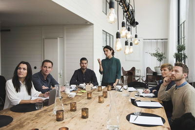 Female business professional explaining to colleagues during meeting at table in office