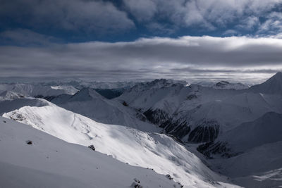 Scenic view of snow covered mountains against cloudy sky