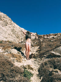 Rear view of woman walking on mountain against clear blue sky