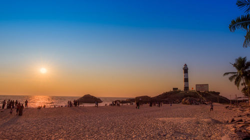 People on beach against clear sky during sunset