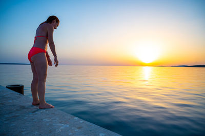 Full length of woman standing in sea against sky during sunset