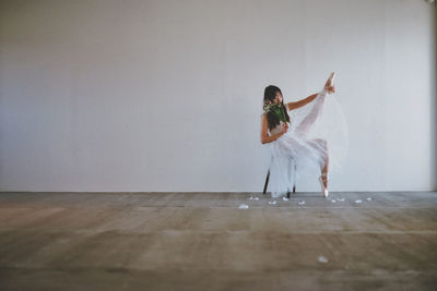 Full length of woman dancing on hardwood floor against wall