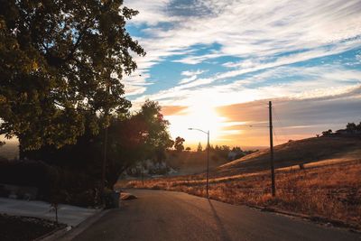 Empty road by trees against sky during sunset