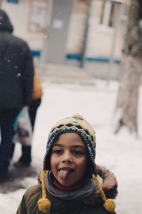 Girl sticking out tongue while standing outdoors during winter