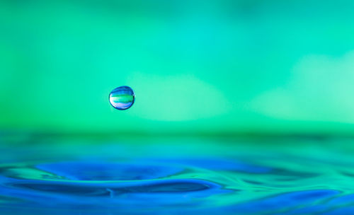 Close-up of drop falling on water surface against turquoise background