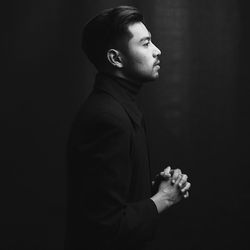 Side view of young man looking away against black background