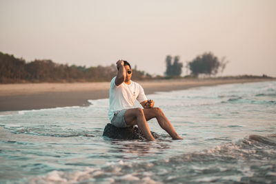 Side view of young woman sitting at beach