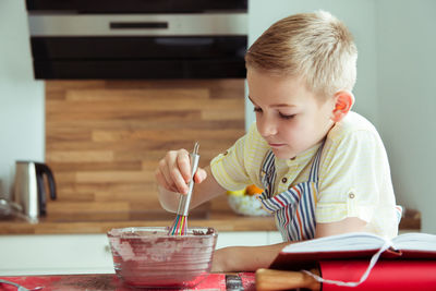 Cute boy preparing food while reading recipe in book