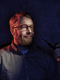 Smiling mature man looking away while smoking on chair in darkroom at home