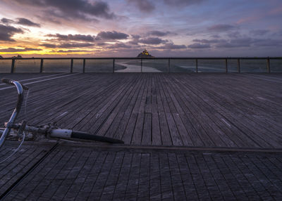 Empty footpath by sea against sky during sunset