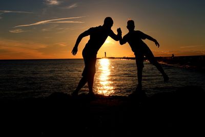 Silhouette men on beach against sky during sunset