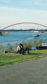 Man sitting on bridge over river against sky