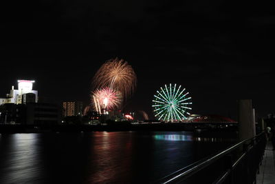 Illuminated ferris wheel by river at night