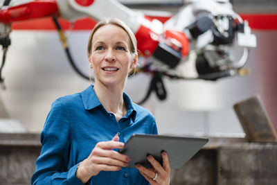 Contemplative engineer holding tablet pc in robot factory