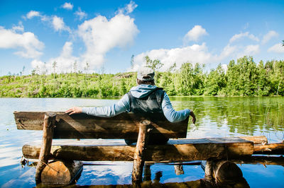 Man sitting on wood by lake against sky