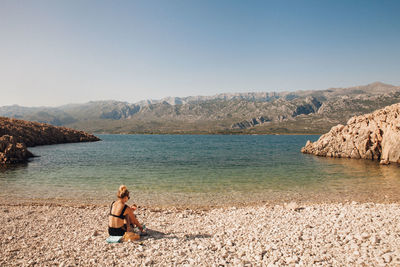 Rear view of woman sitting on shore at beach