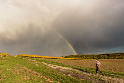 Scenic view of rainbow and child with an umbrella over field