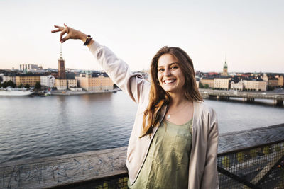 Portrait of smiling young woman standing against river in city