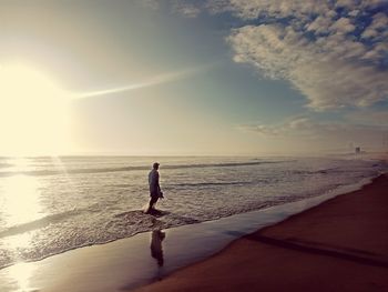 Rear view of man walking at beach against sky during sunset