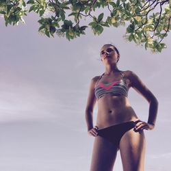 Low angle view of young woman standing at beach against sky