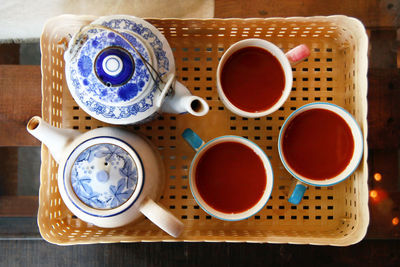 Top view on a plastic tray with two white-blue teapots and cups with thai tea on a glass table.