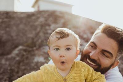 Portrait of toddler with father looking and smiling while sitting on rock formation