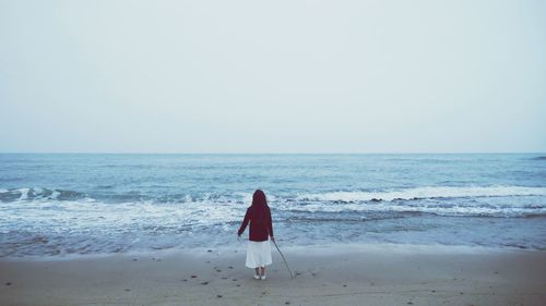 Rear view of woman wearing hood while standing at beach against sky