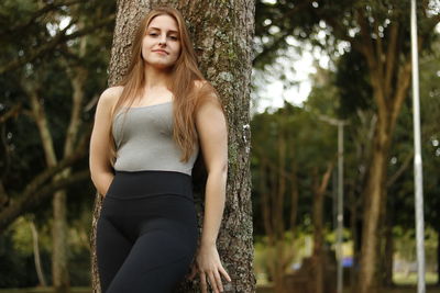 Portrait of beautiful woman standing by tree at park