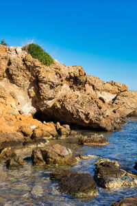 Rock formations by sea against clear blue sky