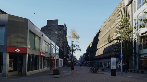 Road by buildings against clear sky in city