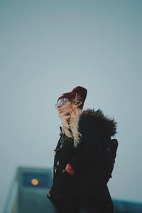 Low angle view of thoughtful young woman wearing warm clothing against clear sky