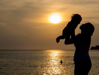 Silhouette of female holding little girl at sunset sun reflection in sea surface