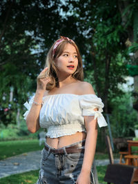 Beautiful young woman looking away while standing against trees