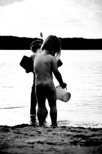 Rear view of shirtless boy at beach against sky