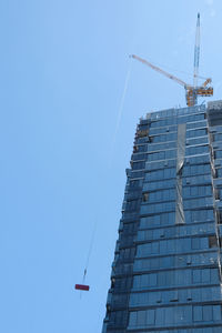 Low angle view of crane by building against clear blue sky