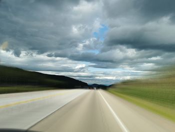 Road passing through landscape against cloudy sky