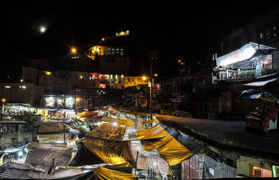 People in illuminated city against sky at night