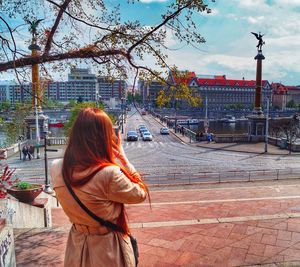 Rear view of woman standing against sky in city