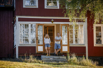 Full length portrait of couple standing at doorway of log cabin